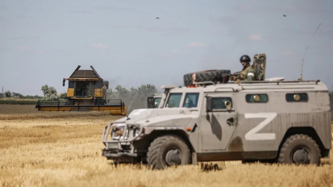 Броньовик з літерою Z біля комбайна на полі під час мобілізації в Росії