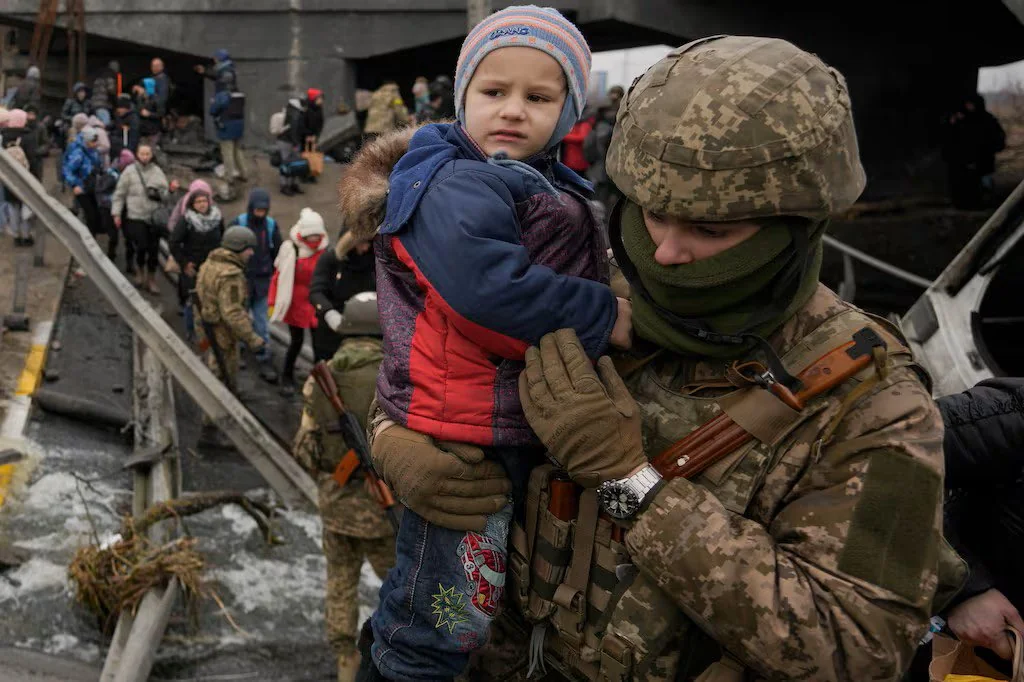 Військовий у камуфляжі тримає маленьку дитину на руках під мостом серед евакуйованих