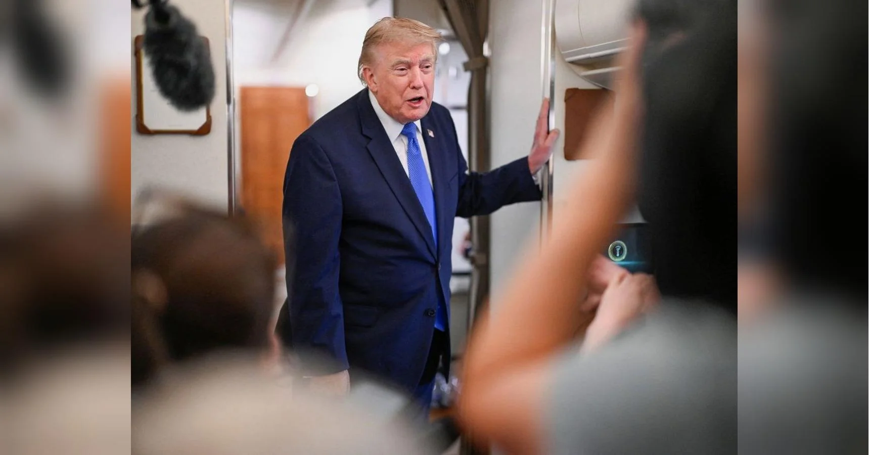 Дональд Трамп у синьому костюмі розмовляє з журналістами всередині літака